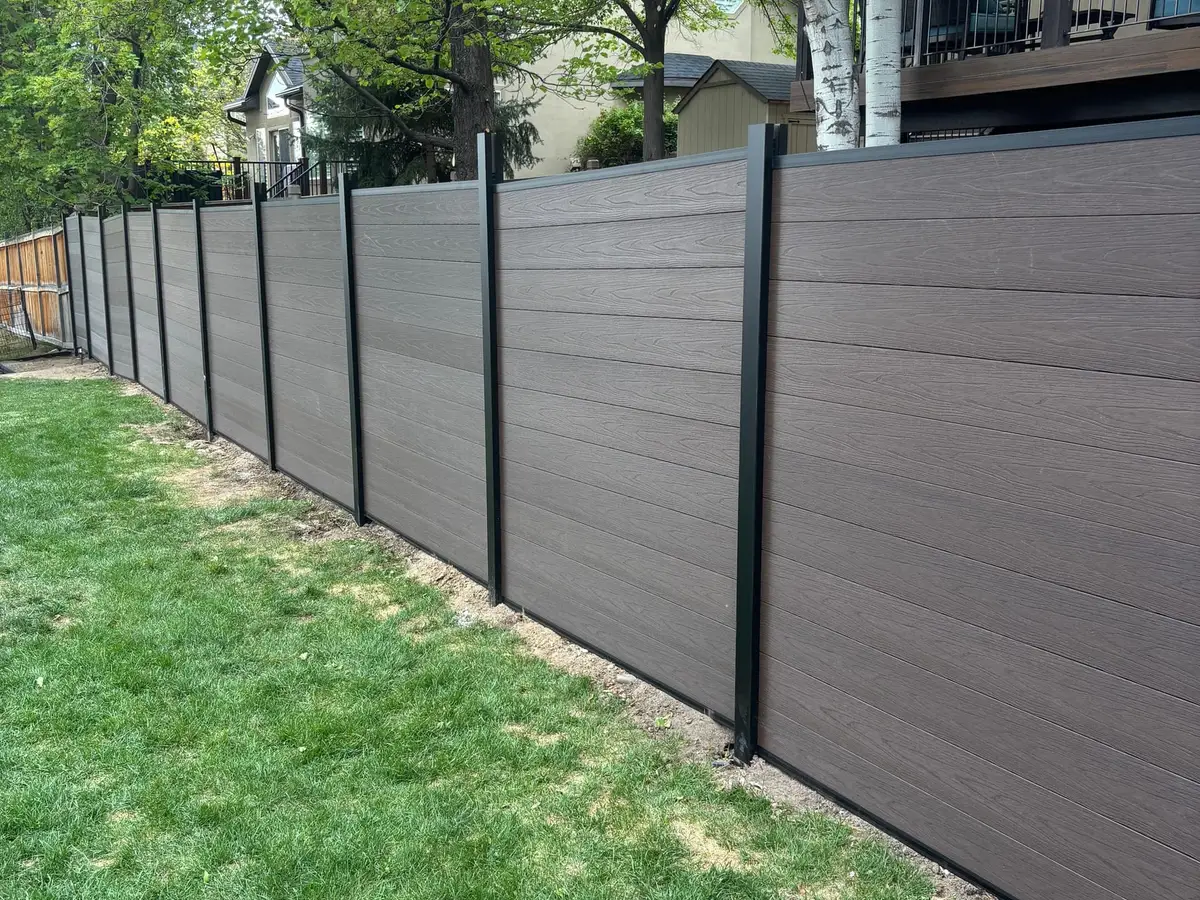 Dark composite fence running along a lawn under mature trees
