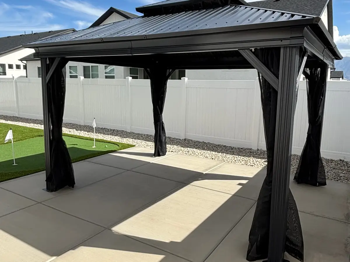 Black steel gazebo on a concrete pad beside a putting green