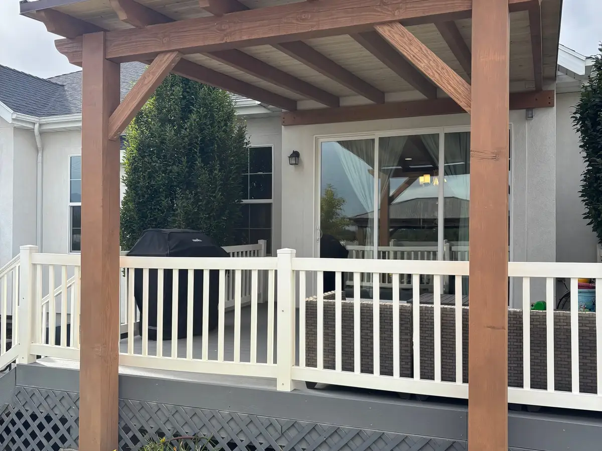 Cedar pergola over a deck with white railing behind a home